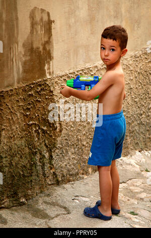 Petit Garçon jouant avec son pistolet à eau éclaboussant les murs avec de l'eau dans le village de Vrbnik sur l'île croate de Krk, sur la mer Adriatique Banque D'Images