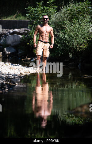 Beau jeune modèle soyons forts à l'extérieur et Flexing Muscles musculaire Bodybuilder - Athletic Man Posing Banque D'Images