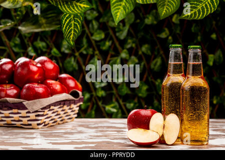 Deux bouteilles de boissons cidre froid nice debout près de bol tressé avec des pommes mûres sur la table dans le jardin Banque D'Images