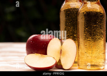 Deux bouteilles de boissons cidre froid nice debout près de bol tressé avec des pommes mûres sur la table dans le jardin Banque D'Images