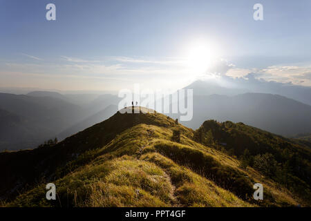 Deux hommes debout sur le dessus de la montagne couverte d'herbe regarder superbe panorama au coucher du soleil Banque D'Images
