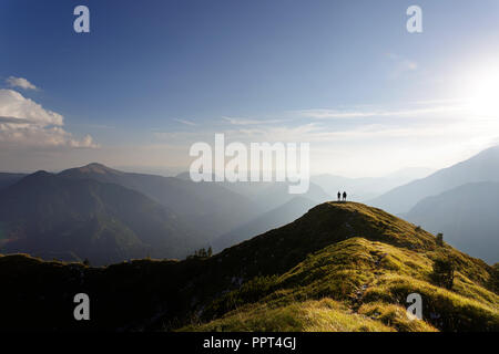 Deux hommes debout sur le dessus de la montagne couverte d'herbe regarder superbe panorama au coucher du soleil Banque D'Images