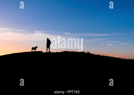 Un homme et son chien vu en silhouette contre un coucher de soleil colorés à Newquay en Cornouailles. Banque D'Images