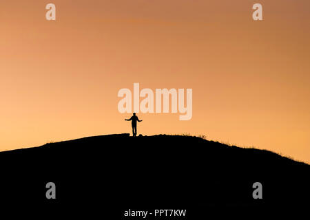 La figure d'un Walker silhouetté contre un coucher de soleil intense sur l'Est à Newquay Pentire à Cornwall. Banque D'Images