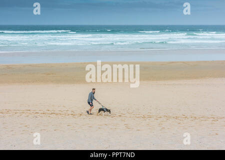 Un homme promenait son chien sur une plage de Fistral à Newquay en Cornouailles. Banque D'Images