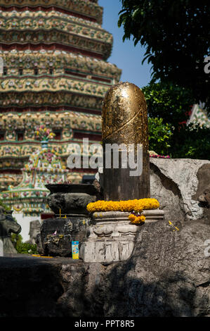 Couvert de feuilles d'or phallus statue avec guirlande de fleurs et d'autres offrandes dans le parc du Wat Pho (Temple du Bouddha couché), Bangkok Banque D'Images