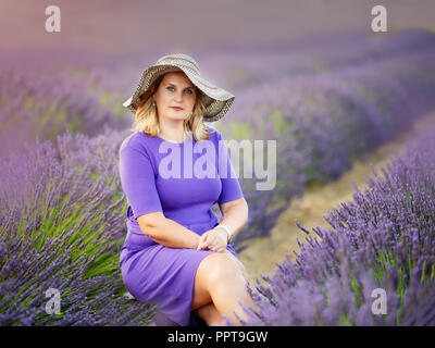 Belle jeune femme dans un beau chapeau dans les champs de lavande Banque D'Images