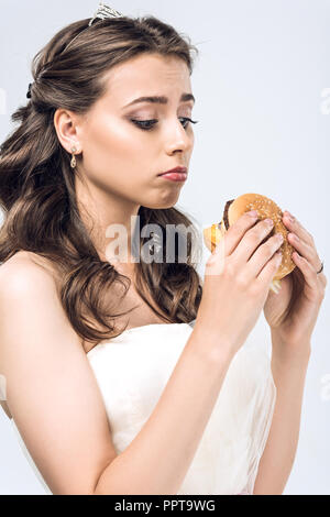 Triste jeune mariée robe de mariage en regardant burger en mains isolated on white Banque D'Images