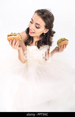 Portrait of attractive young mariée robe de mariage en tenant des hamburgers dans les mains on white Banque D'Images