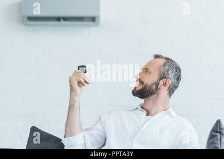 Homme barbu d'allumer l'air conditionné avec télécommande Banque D'Images