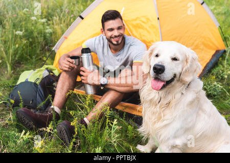 Thermos avec touristiques assis dans la tente jaune avec golden retriever dog Banque D'Images