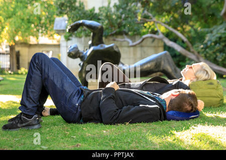 St Paul's, Londres, le 27 septembre 2018. Deux jeunes personnes reposent sur la pelouse à côté de la statue de Thomas Becket par Copnall. Les gens profiter du magnifique soleil d'automne avec des températures chaudes et un ciel bleu, beaucoup de vous détendre sur les pelouses autour de la cathédrale de St Paul, dans la ville de Londres. Credit : Imageplotter News et Sports/Alamy Live News Banque D'Images