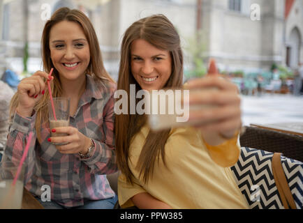 Deux filles gaie joyeuse en tenant une séance tout en selfies at cafe. Heureux les jeunes femmes s'amusant dans un coffee shop. Meilleurs amis de prendre un avec smart selfies Banque D'Images