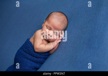 Dormir, neuf jours vieux garçon nouveau-né emmailloté dans un emballage bleu. Tourné dans le studio sur le denim blue matériau. Banque D'Images
