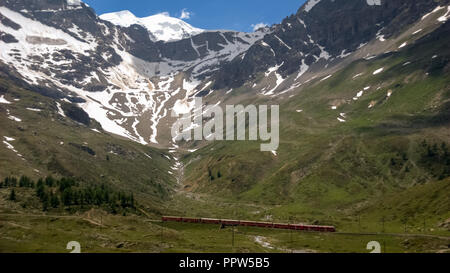 Red train suisse des Chemins de fer rhétiques à cheval sur le col de la Bernina (Grisons, Suisse) à partir de et vers l'Italie. Banque D'Images