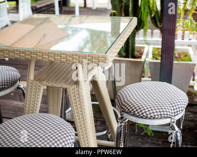 Close up en osier tissu moderne avec table de verre sur le dessus et de l'acier inoxydable chaises avec coussins sur plancher en bois. Match mixte et café rétro. Banque D'Images