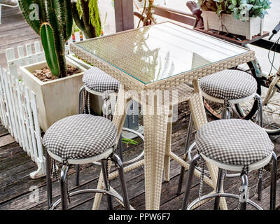 Table en osier tissu moderne avec verre sur le dessus et de l'acier inoxydable chaises avec coussins sur plancher en bois. Match mixte et café rétro. Banque D'Images