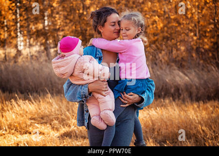 Une jeune femme mère dans une veste jeans robe et tient ses filles et profiter de la nature, posant et à leur parler sur le dos de l'arrière-plan Banque D'Images