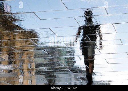 Réflexion floue ombre silhouette dans une flaque d'un jeune homme marchant sur la rue ville pluvieuse après la pluie Banque D'Images