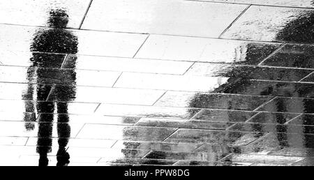 Réflexion floue des silhouettes d'ombre d'un homme marchant sur la rue ville pluvieuse sombre en noir et blanc Banque D'Images