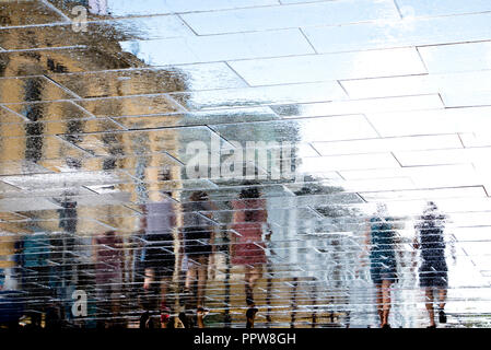 Réflexion floue ombre silhouette dans une flaque de personnes marchant sur la rue ville humide après la pluie Banque D'Images