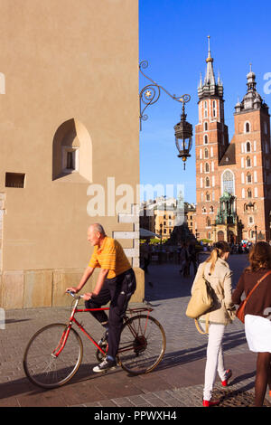 Cracovie, Pologne : un homme du passé des cycles Halle aux draps et la Basilique Sainte-Marie l'Église à la place du marché dans la vieille ville de Cracovie. Banque D'Images