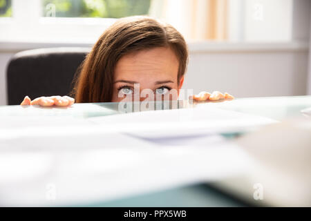 Peur Businesswoman Peeking du bord de Desk In Office Banque D'Images