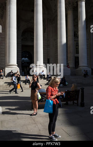 Une dame vérifie les messages sous les piliers du néo-classique Royal Exchange dans la ville de Londres - le centre financier de la capitale (aka le Square Mile), le 27 septembre 2018, à Londres, en Angleterre. Banque D'Images