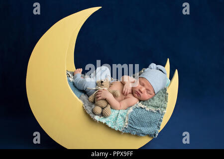 Studio portrait d'un nouveau-né âgé de dix jours en portant des bas de pyjama bébé garçon et un coin couchage. Il est en train de dormir sur une lune posing and holding a prop Banque D'Images