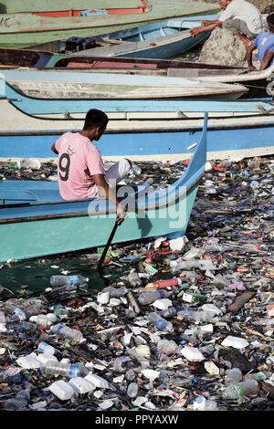 L'homme dans l'eau en bateau taxi à travers les palettes océan plein de sacs en plastique, les bouteilles en plastique, polystyrène et autres ordures dans Semporna, Bornéo, Malaisie Banque D'Images