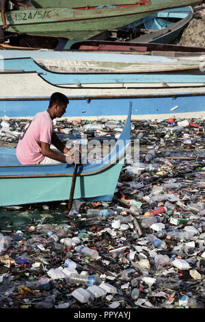 L'homme dans l'eau en bateau taxi à travers les palettes océan plein de sacs en plastique, les bouteilles en plastique, polystyrène et autres ordures dans Semporna, Bornéo, Malaisie Banque D'Images