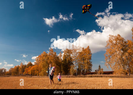 Le concept de famille livestyle et les loisirs de plein air en automne. Une jeune femme avec bébé fille et jouit d'nature et joue avec un cerf-volant sur une chaude autu Banque D'Images