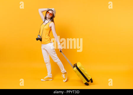 Traveler'femme en été des vêtements décontractés, hat avec valise jaune isolé sur fond orange. Passagère voyageant à l'étranger pour voyager o Banque D'Images