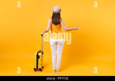 Vue arrière retour femme touristique en été des vêtements décontractés, hat with suitcase attraper une voiture de taxi jaune isolé sur fond orange. Les femmes qui voyagent à l'étranger Banque D'Images