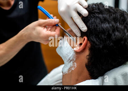 Le jeune homme est d'être rasé avec un rasoir droit dans un salon de coiffure Banque D'Images