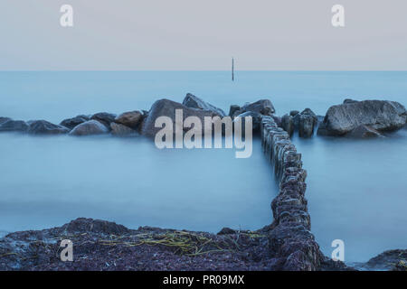 Des pierres sur la rive dans l'eau laiteuse bleuté après le coucher du soleil au cours de l'heure bleue à Rabylille Beach, à l'île de Moen, Danemark, Scandinavie, l'Europe. Banque D'Images