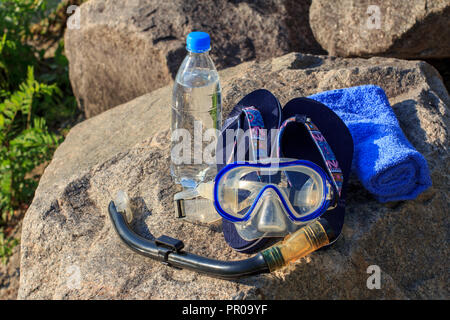 Bouteille avec de l'eau, serviette, tongs, masque et tuba pour la plongée se trouvent sur tube avec pierres mer arrière-plan. L'été, vie active Banque D'Images