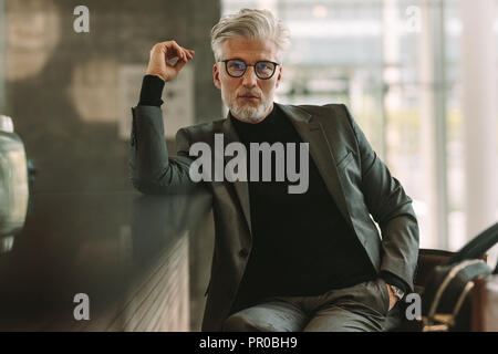 Portrait horizontal de handsome senior businessman sitting at cafe. Costume d'affaires Senior man in looking at camera while sitting at coffee shop. Banque D'Images