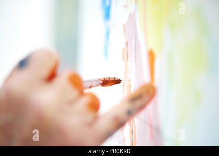 Close up de la main de l'artiste masculin, dessin photo à l'atelier. Teint à la main avec des peintures du peintre, tout en maintenant la peinture et pinceau peinture orange riche peintre en studio. Concept de passe-temps et des gens de talent. Banque D'Images