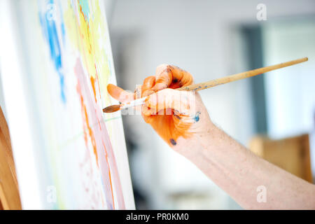 Artiste de main, tenant le pinceau et la peinture orange riche en peinture painter studio. Teint à la main avec des peintures du peintre, dessin photo à l'atelier. Concept de passe-temps et des gens de talent. Banque D'Images