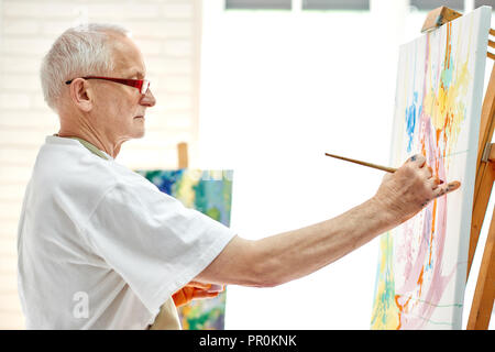 Les créatifs dessin peintre image colorée au studio lumineux. Vue latérale du processus de peinture dans l'art de travail. Artiste masculin en portant des T-shirt blanc et des lunettes modernes, qui travaillent sur de nouveaux chef-d'œuvre. Banque D'Images