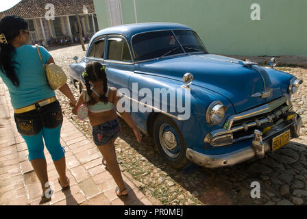 Mère et fille marcher par un blue vintage voiture américaine dans les rues de Trinidad Cuba Antilles Banque D'Images