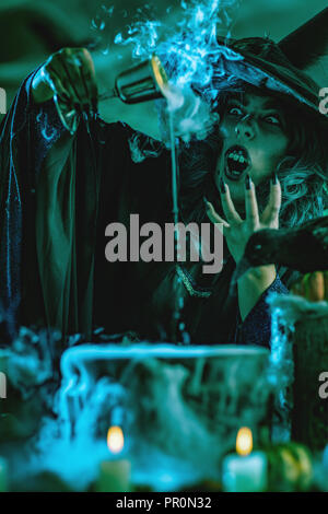 Une sorcière par temps brumeux entourant est titulaire d'une coupe au-dessus de l'eau bouillante pendant la cuisson d'une soupe de poison. Banque D'Images