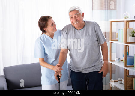 Gardien femelle aider Happy Senior Man tout en marchant à la maison Banque D'Images