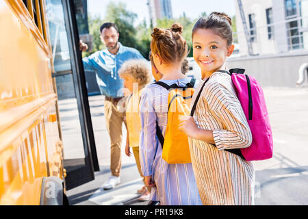 Petite lycéenne qui entrent à l'école avec ses camarades de bus alors que teacher standing près de la porte Banque D'Images