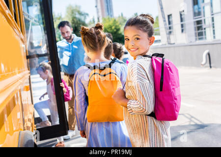 Petite lycéenne qui entrent à l'école avec ses camarades de bus alors que teacher standing près de la porte Banque D'Images