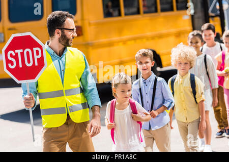 Beau garde du trafic routier de passage avec des élèves en face de school bus Banque D'Images