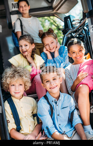 Groupe d'adorables élèves assis dans les escaliers de l'autobus scolaire et looking at camera Banque D'Images