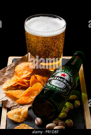 Londres, Royaume-Uni - 26 septembre 2018 : Bouteille de verre avec de la bière Heineken et snack-ostone board sur noir. Pistaches et de bretzel et plaquettes Banque D'Images