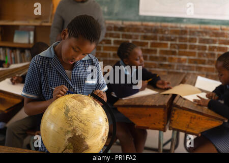 Schoolboy looking at globe in classroom Banque D'Images